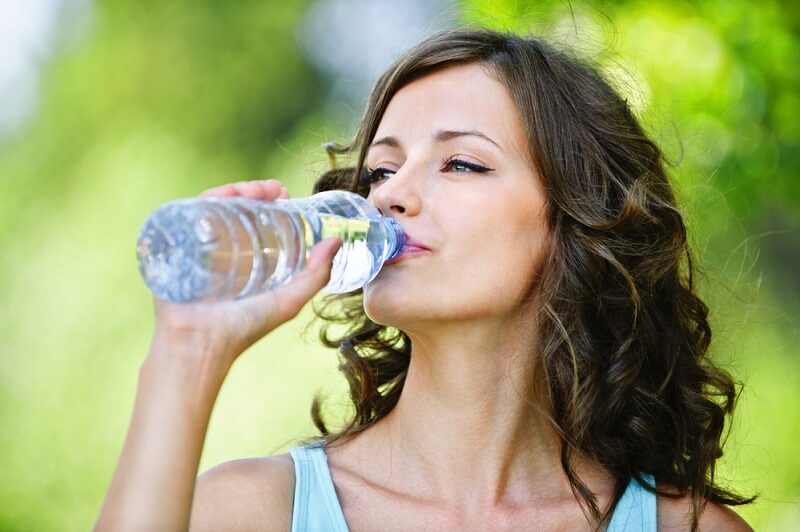 portrait-of-young-beautiful-dark-haired-woman-wearing-blue-t-shirt-drinking-water-at-summer-green-park